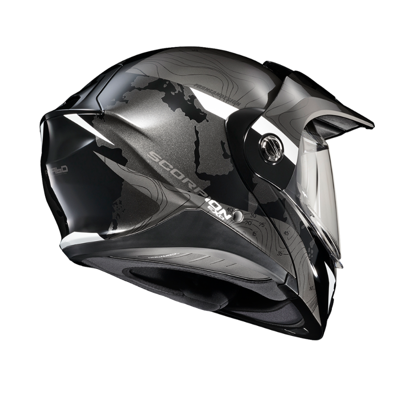 Rear three-quarter view of the Scorpion EXO-AT960 Topographic Modular Adventure Motorcycle Helmet in Black/White. The helmet features a matte black and metallic grey finish with subtle topographic map graphics and contrasting white accent panels. Visible are the aerodynamic rear spoiler, advanced ventilation ports, adventure peak visor, and clear EverClear® face shield. Designed for both on-road touring and off-road adventure riding, the EXO-AT960 combines aggressive styling, premium comfort, and rugged all
