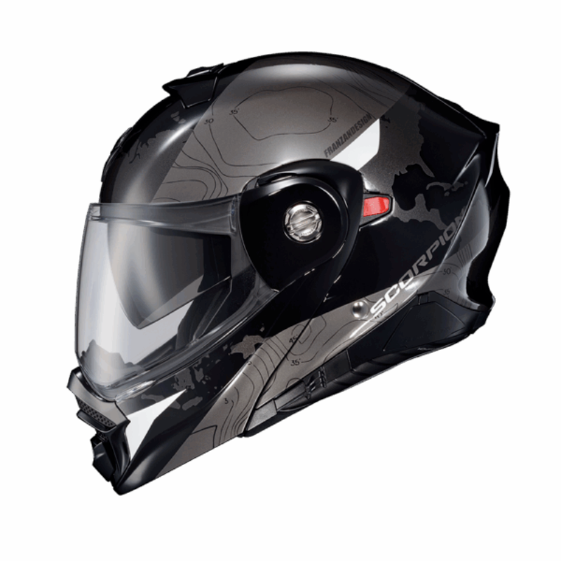 Side profile of the Scorpion EXO-AT960 Topographic Modular Adventure Motorcycle Helmet in Black/White. This adventure touring helmet features a sleek matte black and metallic grey finish with subtle topographic contour graphics and contrasting white accent panels. Equipped with a clear EverClear® face shield, integrated SpeedView® drop-down sun visor, aerodynamic shell design, and modular flip-up chin bar, the EXO-AT960 is built for long-distance touring and off-road adventure riding, offering premium comfo
