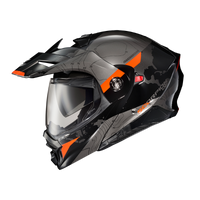 Scorpion EXO-AT960 Topographic Modular Adventure Motorcycle Helmet in Black/Orange. This adventure-style modular helmet features a matte black and grey topographic map graphic with bold orange accent panels on the peak visor, chin bar, and sides. Equipped with an aerodynamic adventure peak, clear EverClear® face shield, integrated drop-down sun visor, and flip-up modular chin bar, the EXO-AT960 is designed for both touring and off-road riding. The aggressive styling, advanced ventilation, and premium safety
