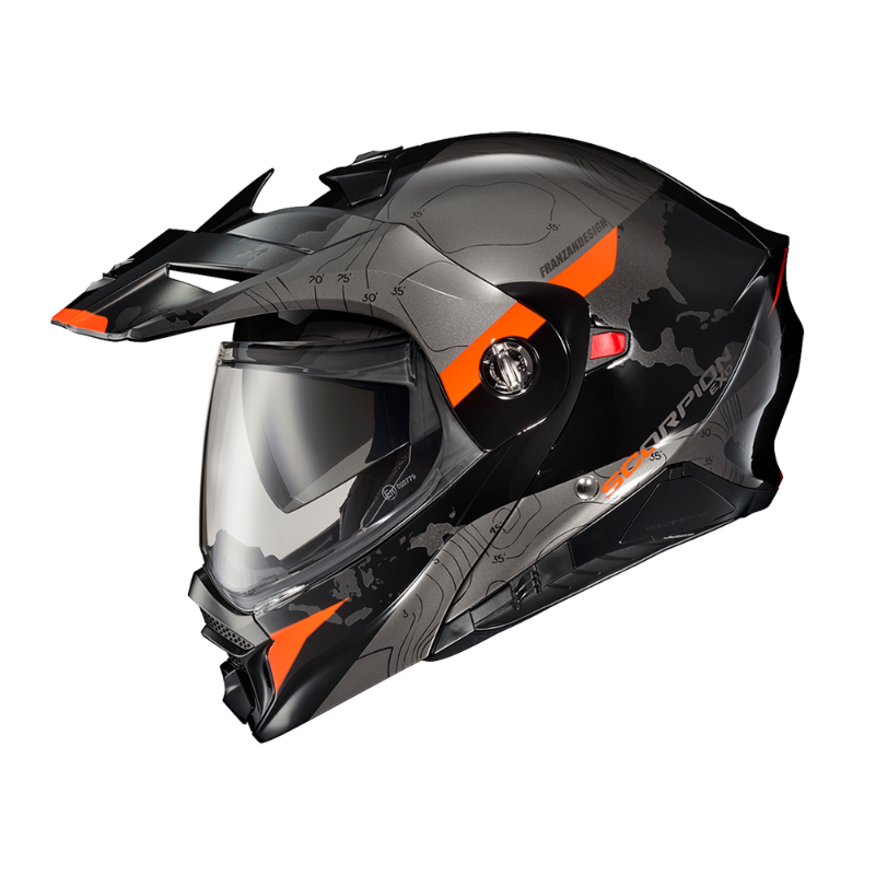 Scorpion EXO-AT960 Topographic Modular Adventure Motorcycle Helmet in Black/Orange. This adventure-style modular helmet features a matte black and grey topographic map graphic with bold orange accent panels on the peak visor, chin bar, and sides. Equipped with an aerodynamic adventure peak, clear EverClear® face shield, integrated drop-down sun visor, and flip-up modular chin bar, the EXO-AT960 is designed for both touring and off-road riding. The aggressive styling, advanced ventilation, and premium safety