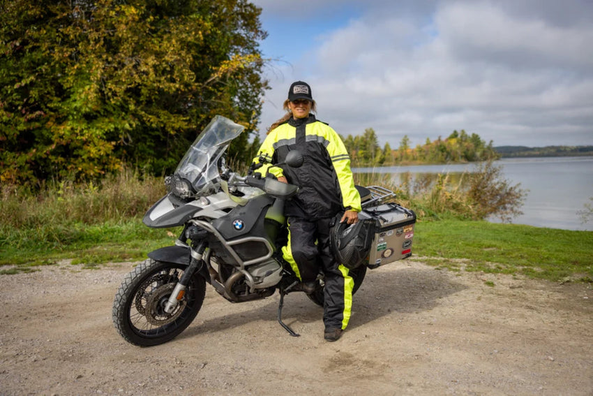 Lifestyle image of a rider wearing the Gryphon Coastal Rain Suit in high-visibility yellow and black beside an adventure motorcycle. The waterproof motorcycle rain jacket and pants provide all-weather protection, reflective visibility, and full-coverage comfort for touring, commuting, and long-distance adventure riding.