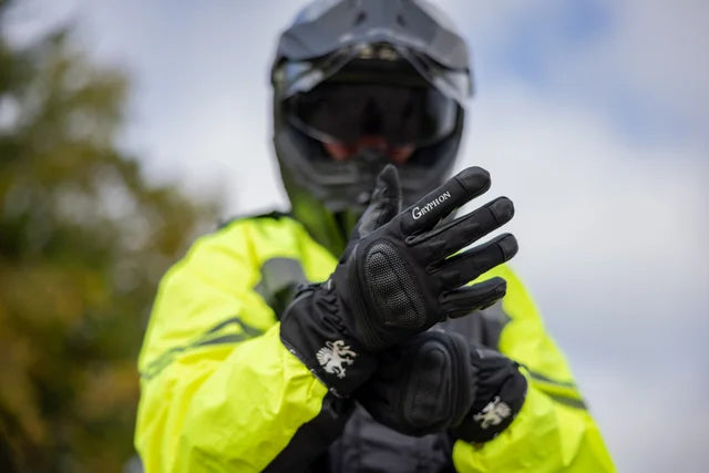 Person wearing a bright yellow jacket, and Gryphon Amazon black waterproof motorcycle gloves, and a helmet outdoors.