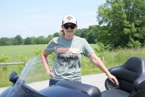 Person wearing a cap and sunglasses wearing a green Gryphon Any Road Any Ride T-shirt outdoors with greenery in the background