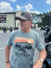 Man wearing a t-shirt with a motorcycle graphic and 'Gryphon' branding, standing in a parking lot with motorcycles.