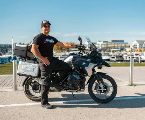 Person standing next to a motorcycle wearing a Black Gryphon branded T-Shirt in an outdoor setting with clear skies
