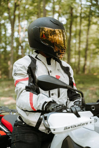 Person wearing a helmet and a grey Gryphon Blue Ridge Motorcycle jacket  on a motorcycle in a forest setting