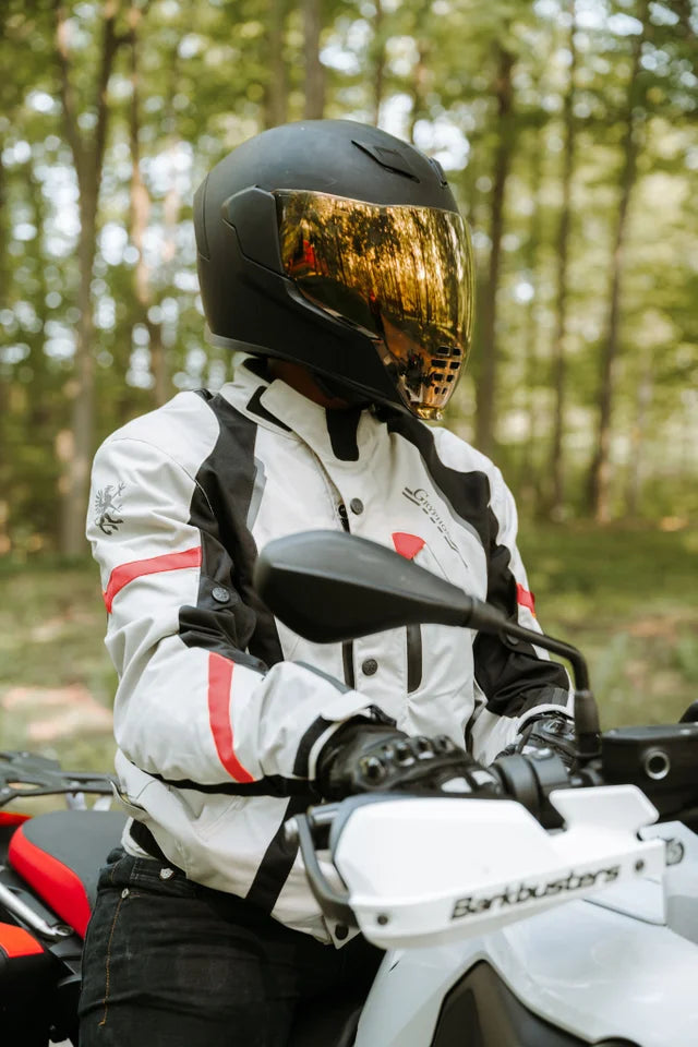 Person wearing a helmet and a grey Gryphon Blue Ridge Motorcycle jacket  on a motorcycle in a forest setting