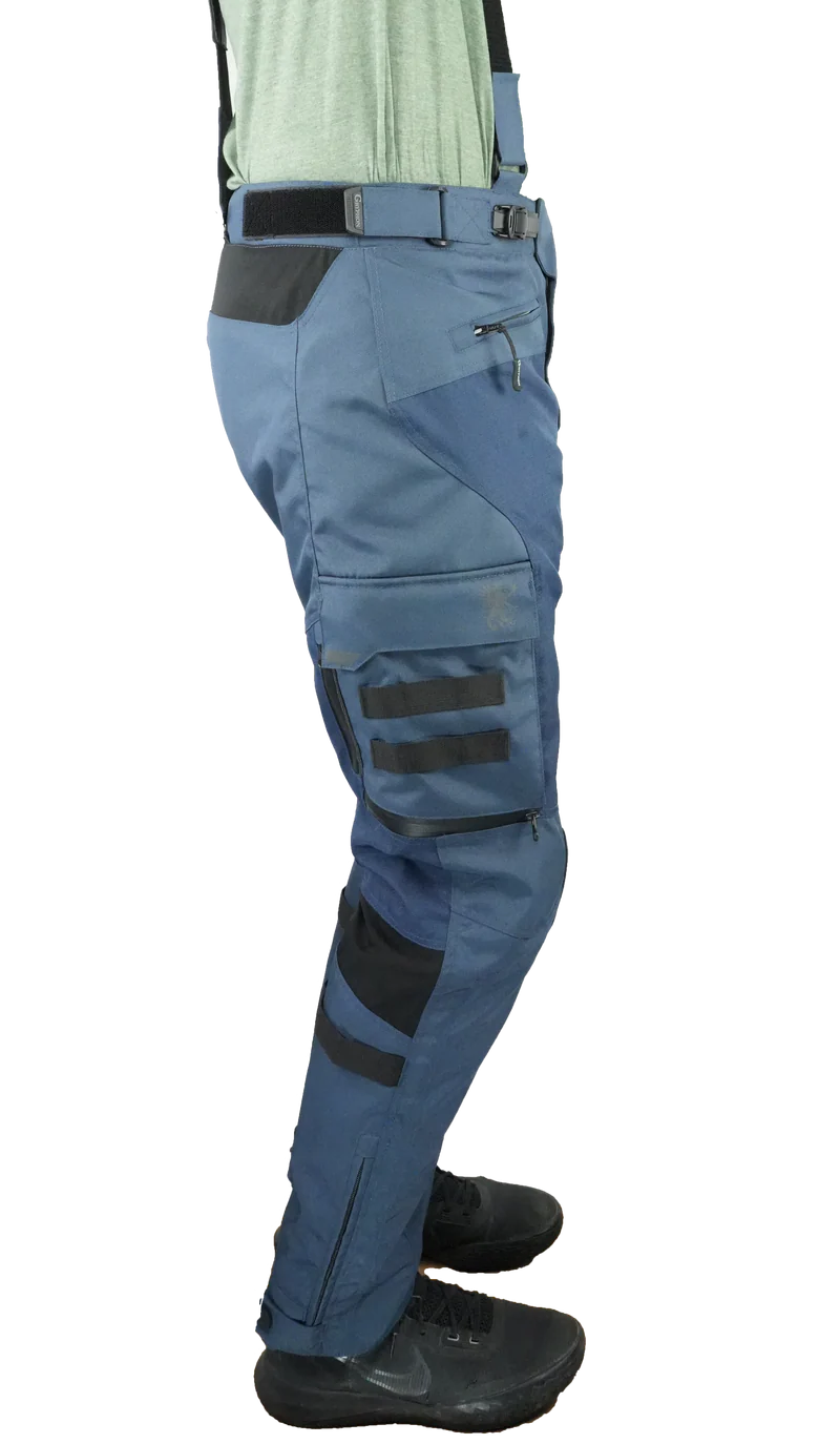 Right-side view of Gryphon Single Track Waterproof Motorcycle Pants in blue. These adventure riding pants feature a durable waterproof textile construction, removable suspenders, adjustable waist buckle, zippered hand pocket, large cargo pocket with MOLLE webbing and Gryphon logo, reinforced knee panels, articulated fit for riding comfort, and zippered lower leg openings for easy boot access. Designed for touring, dual-sport, and off-road motorcycle adventures in all weather conditions.