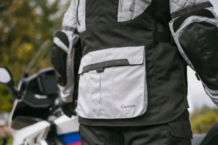 Person wearing a black and gray motorcycle jacket with a visible brand logo, standing next to a motorcycle.