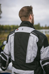 Person wearing a black and gray motorcycle jacket with a logo on the back, standing outdoors.