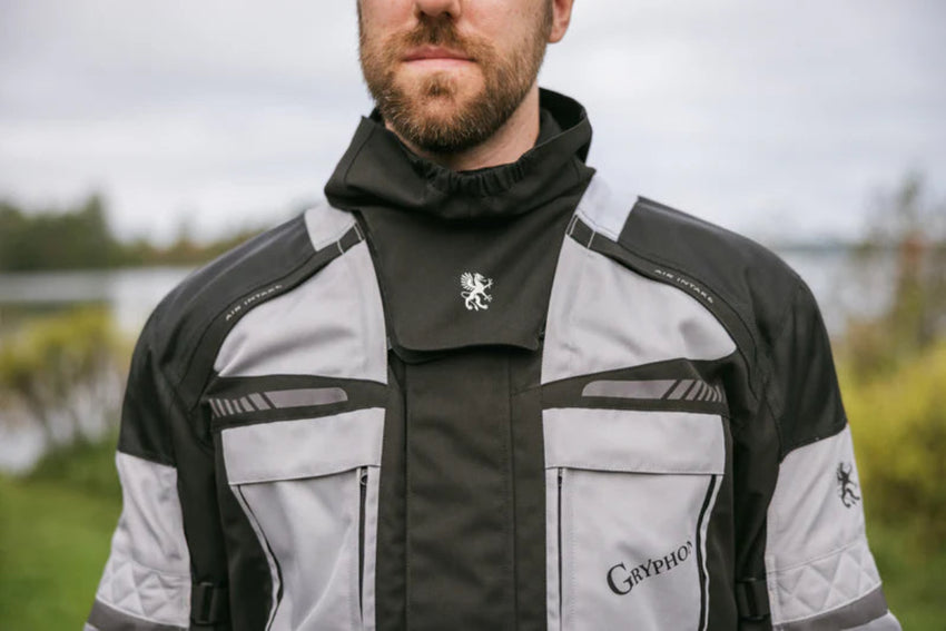 Man wearing a black and gray jacket with a logo, standing outdoors.