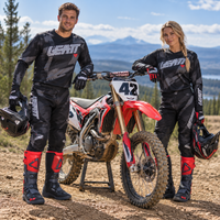 Man and woman wearing LEATT 3.5 MX motocross boots in black and red with full motocross riding gear, standing beside an MX dirt bike in an outdoor off-road setting.