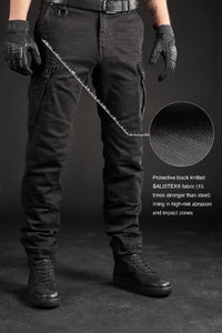 Person wearing black motorcycle cargo pants with text detailing material and features on a dark background