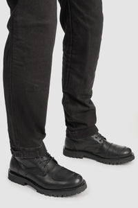 Person wearing black leather boots and black pants on a white background