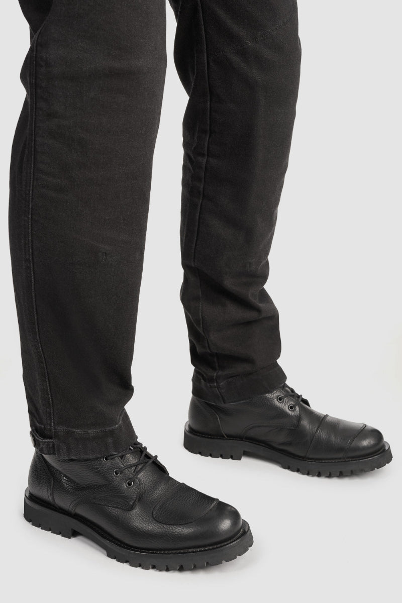 Person wearing black leather boots and black pants on a white background