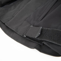 Close-up detail of a black tactical jacket or vest showing a hook-and-loop strap closure and fabric texture against a white background.