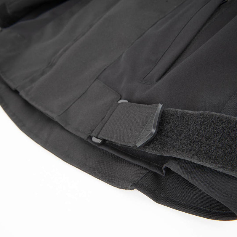 Close-up detail of a black tactical jacket or vest showing a hook-and-loop strap closure and fabric texture against a white background.