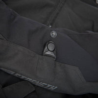 Close-up of black technical outerwear fabric with a snap button, a black plastic hook-and-loop closure, and partial visible gray 'STRENGTH' branding on the lower side.