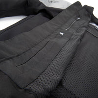 Close-up detail of a black technical jacket showing a zippered pocket, mesh fabric panel, and stitched construction.