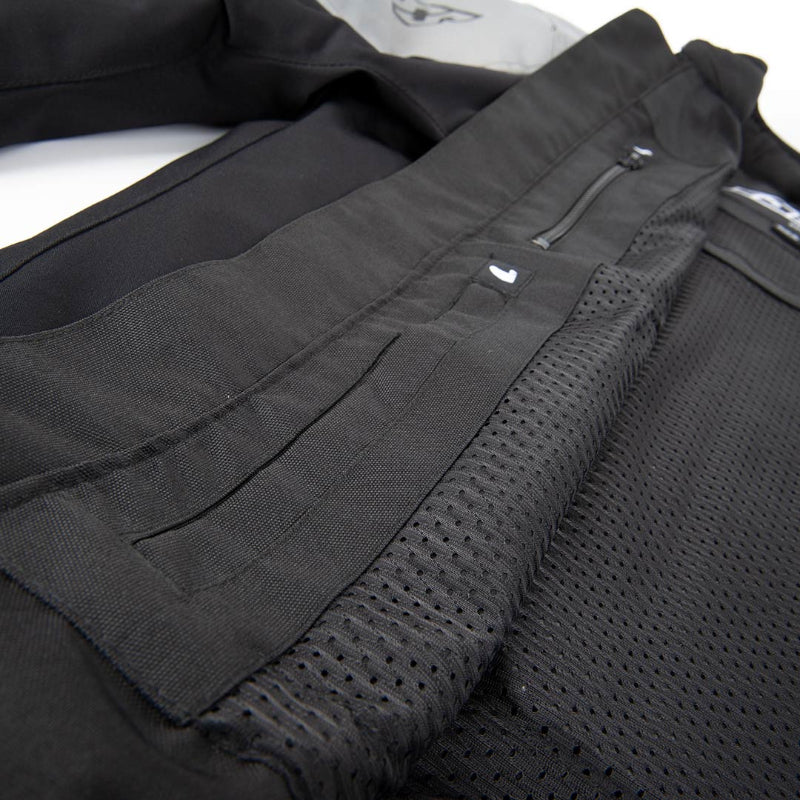 Close-up detail of a black technical jacket showing a zippered pocket, mesh fabric panel, and stitched construction.