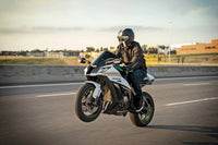 A rider wearing a black helmet and leather riding gear maneuvers a white and black sport motorcycle on an open road during golden hour.