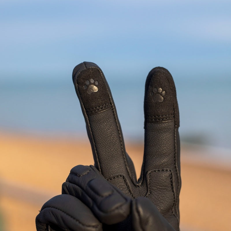 Close-up of MotoGirl Bessie black motorcycle glove showing touchscreen-compatible index and middle fingertips with distinctive paw-print detailing.