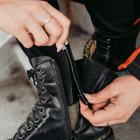Close-up of MotoGirl ISLA black motorcycle jeans showing the ankle zipper being opened over a black lace-up boot for easy adjustment and comfortable wear