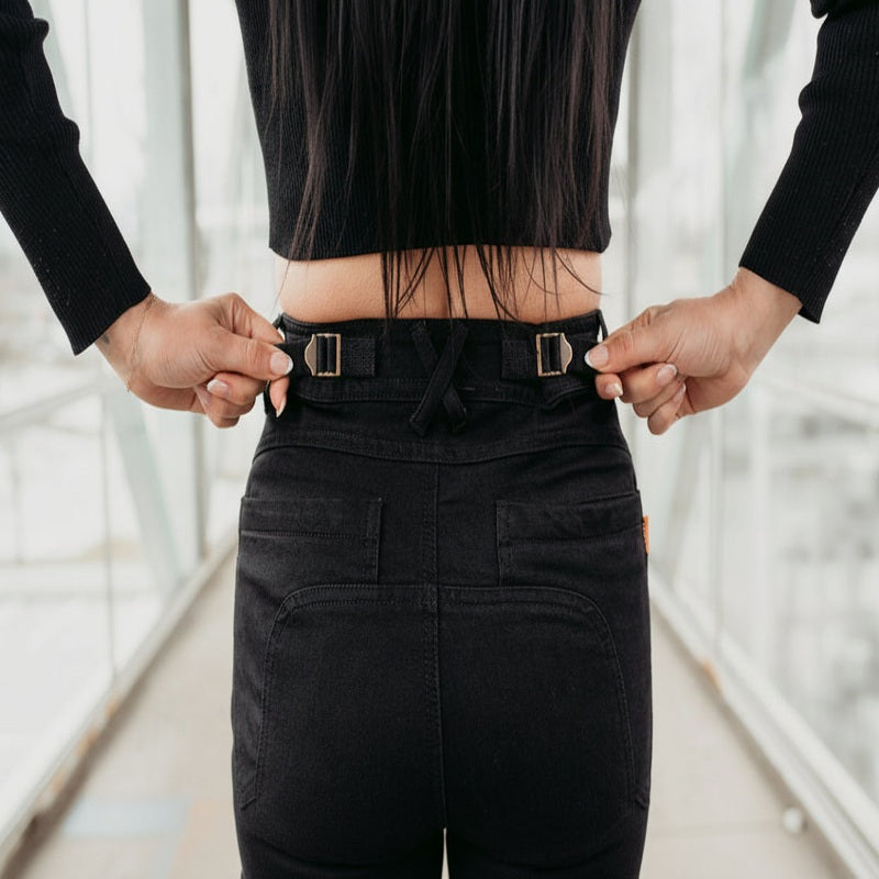 Rear close-up of MotoGirl ISLA black women's motorcycle jeans showing adjustable waist straps with metal buckles, belt loops and back pockets for a customizable fit.
