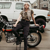 A person sitting on a black motorcycle wearing Motogirl branded black cargo trousers and a green t-shirt.