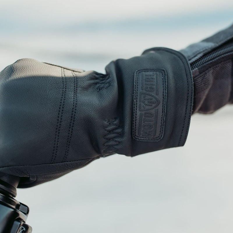 lose-up of black MotoGirl Nandi motorcycle glove showing leather stitching, wrist strap and textured construction while resting on a motorcycle handlebar.