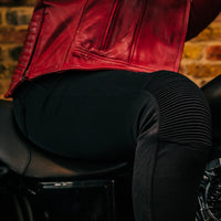 Person wearing a red leather jacket sitting on a motorcycle with a brick wall background