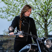 a girl wearing a MotoGirl branded black Sherrie motorcycle jacket standing next to a motorcycle with a nature background