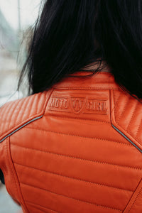 a girl with black hair wearing an orange Motogirl branded Amelia Leather jacket