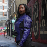 Woman wearing a branded Motogirl Amelia Leather jacket in purple on a city street with graffiti in the background