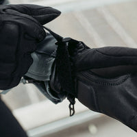 Close-up of the MotoGirl Amina Women's Motorcycle Glove featuring the adjustable hook-and-loop wrist closure being tightened for a secure fit. The premium leather cuff and stretch textile construction provide comfort, protection, and a customizable fit, helping keep the glove securely in place while riding.