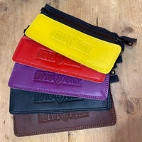 A collection of MotoGirl jacket belt connectors in various solid colors, including black, purple, red, yellow, and brown, laid out on a wooden surface.