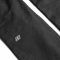 Close-up of black fabric with a small white embroidered double-S logo, shown against a white background.