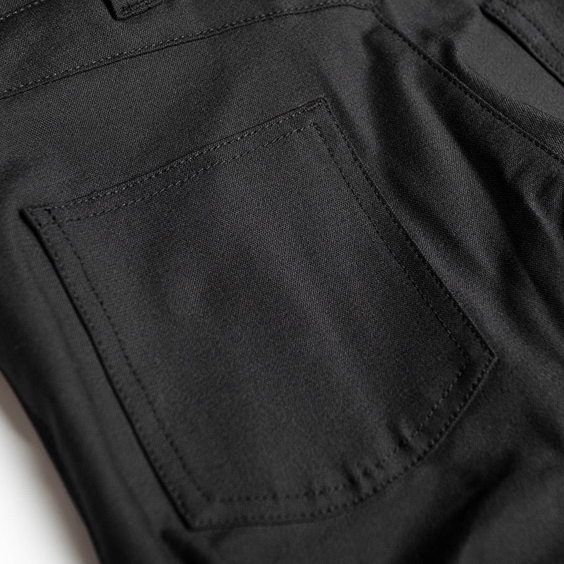 Close-up detail of a black fabric garment showing a stitched pocket and dark woven texture.