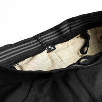 Close-up of the waistband of black trousers, showing the black elastic with gray stripes, a beige inner lining, and a small black size tag.