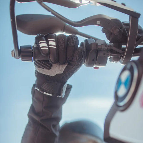 Rider wearing Gryphon Sahara Vented Motorcycle Gloves while gripping the handlebar of an adventure motorcycle. The black and grey summer riding glove features breathable 3D mesh construction, TPU knuckle protection, reinforced leather palm, and touchscreen-compatible fingertips. Shown in a real-world riding position, the glove provides excellent grip, ventilation, and comfort for warm-weather street and adventure motorcycle riding.
