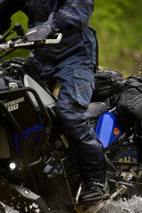 Rider wearing Gryphon Single Track Waterproof Motorcycle Pants and matching adventure jacket while riding a Yamaha Ténéré 700 through water on an off-road trail. The blue waterproof pants feature reinforced knee protection, cargo pockets, adjustable lower legs, and a durable adventure-ready design built for long-distance touring, dual-sport riding, and rugged off-road conditions.