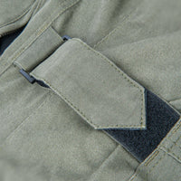 Close-up detail of an olive green canvas waist adjustment and a dark gray hook-and-loop fastener.