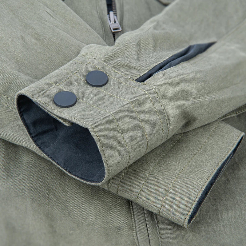 Close-up of an olive green jacket sleeve with two dark snap buttons, a dark blue inner lining, and a zipper, shown against a matching fabric background.