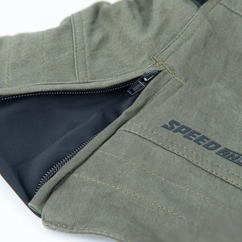 Close-up of an olive green textile product, likely a jacket or vest, showing a zipper opening, dark interior lining, and a stitched 'SPEED' brand mark on the fabric.