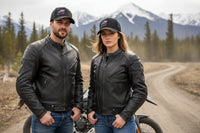 Two people wearing leather jackets and YMGA ball caps in black standing on a dirt road with mountains in the background.