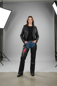 A pair of YMGA branded black leather chaps for women with a pink and black fireweed flower embroidered design on the upper left leg.