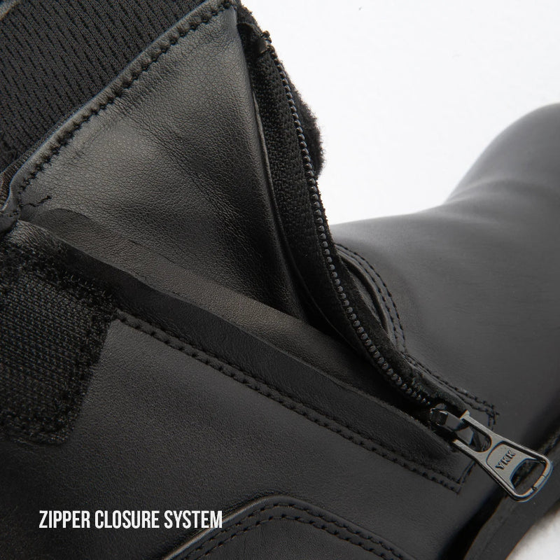 Close-up of a black leather boot showing a zipper closure system with a metal pull tab labeled 'VEE' and a text overlay reading 'ZIPPER CLOSURE SYSTEM'.