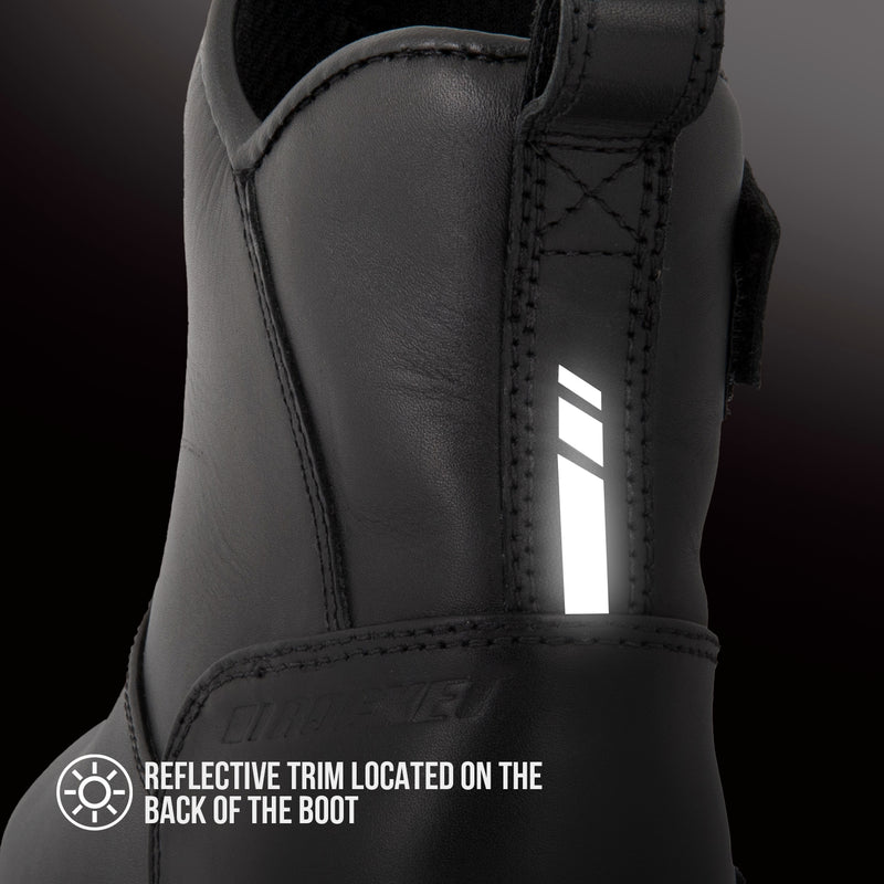 Close-up of a black ankle boot showing a reflective vertical trim on the back panel, with text reading 'REFLECTIVE TRIM LOCATED ON THE BACK OF THE BOOT'.