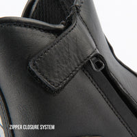 Close-up of a black leather ankle boot showing the zipper closure system with a hook-and-loop strap and metal zipper pull, on a white background with text reading 'ZIPPER CLOSURE SYSTEM'.