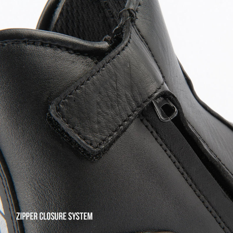 Close-up of a black leather ankle boot showing the zipper closure system with a hook-and-loop strap and metal zipper pull, on a white background with text reading 'ZIPPER CLOSURE SYSTEM'.